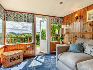 A cozy room with a wooden interior, a sofa, a wicker chest, and a view of greenery outside. - 3 Bed in Taunton (oc-92587) (Brompton Ralph)