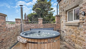 Ein hölzernes Whirlpool mit integriertem Sitz, umgeben von Steinmauern und einem Backsteinzaun.