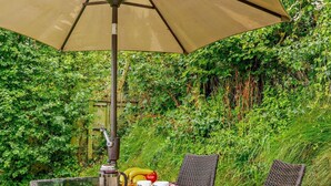Un espace de restauration en plein air avec une table dressée pour deux personnes, une cafetière et une bouteille d’eau.