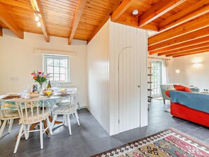 A dining area with a table set for two, a white door, and a red sofa in the adjacent room. - 3 Bed in Haverfordwest (oc-92674) (Solva)