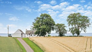 Paesaggio rurale con una casa colonica, campi e alberi.