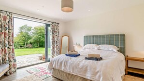 Ein Schlafzimmer mit einem Bett, einem Spiegel, einem Nachttisch und Blick auf einen Garten durch eine Glastür.