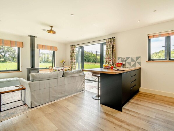 A modern kitchen with a central island, a dining area with a sofa, and large windows offering a view of the outdoors.