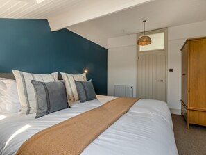 A bedroom with a bed, pillows, a blanket, a wooden wardrobe, a radiator, and a ceiling light. - 1 Bed in Braunton (oc-92737) (Croyde)