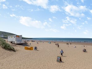 A beach with a lifeguard station, a sign indicating a swimming area, and a beachgoer walking. - 1 Bed in Braunton (oc-92737) (Croyde)