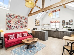 A spacious loft with a high ceiling, exposed wooden beams, a red sofa with patterned cushions, a wooden coffee table, and a kitchen area with a large island. - 1 Bed in Ludlow (oc-92768) (Hayton's Bent)