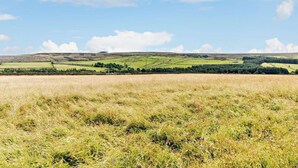 Un paysage rural avec des collines douces, un champ et un bâtiment situé au sommet d’une colline au loin.