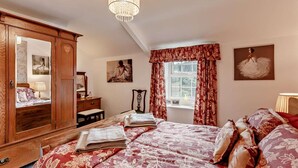 Une chambre à coucher avec un grand lit, une armoire en bois, un miroir, une commode et un lustre.