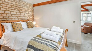 Ein Schlafzimmer mit Backsteinwand, Holzbalken, einem Bett mit weißer Bettwäsche und Blick in einen anderen Raum.