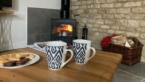 Ein gemütliches Zimmer mit Kamin, zwei gemusterte Tassen, einem Teller Kekse und einem Korbkistchen mit Holzscheiten.