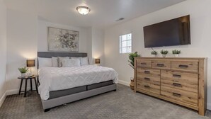 Een slaapkamer met een bed, nachtkastjes, een dressoir, een flatscreen televisie en een plafondlamp.