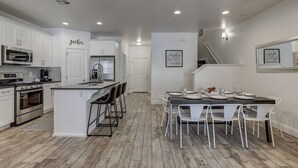 Een moderne keuken met witte kasten, een centraal eiland en een eethoek met een donker houten tafel en witte stoelen.