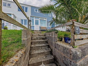 A residential building with a staircase leading to a door, a wooden fence with the number 53, and a palm tree in the background. - 3 Bed in Brixham (oc-92770) (Brixham)