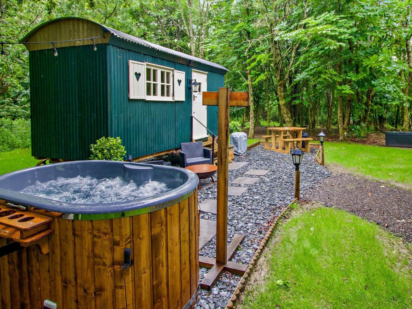 A hot tub, wooden deck, and a small shed in a lush garden setting.