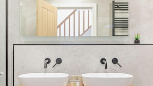 Un baño con dos lavamanos, un mueble de tocador de madera, un espejo y una pequeña planta en maceta.