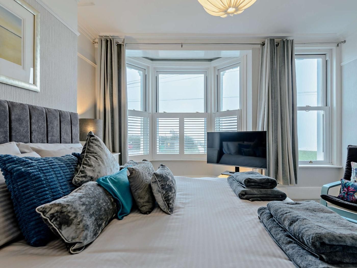 A hotel room with a large bed, a television, and a view of the city through large windows.
