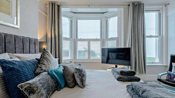A hotel room with a large bed, a television, and a view of the city through large windows.