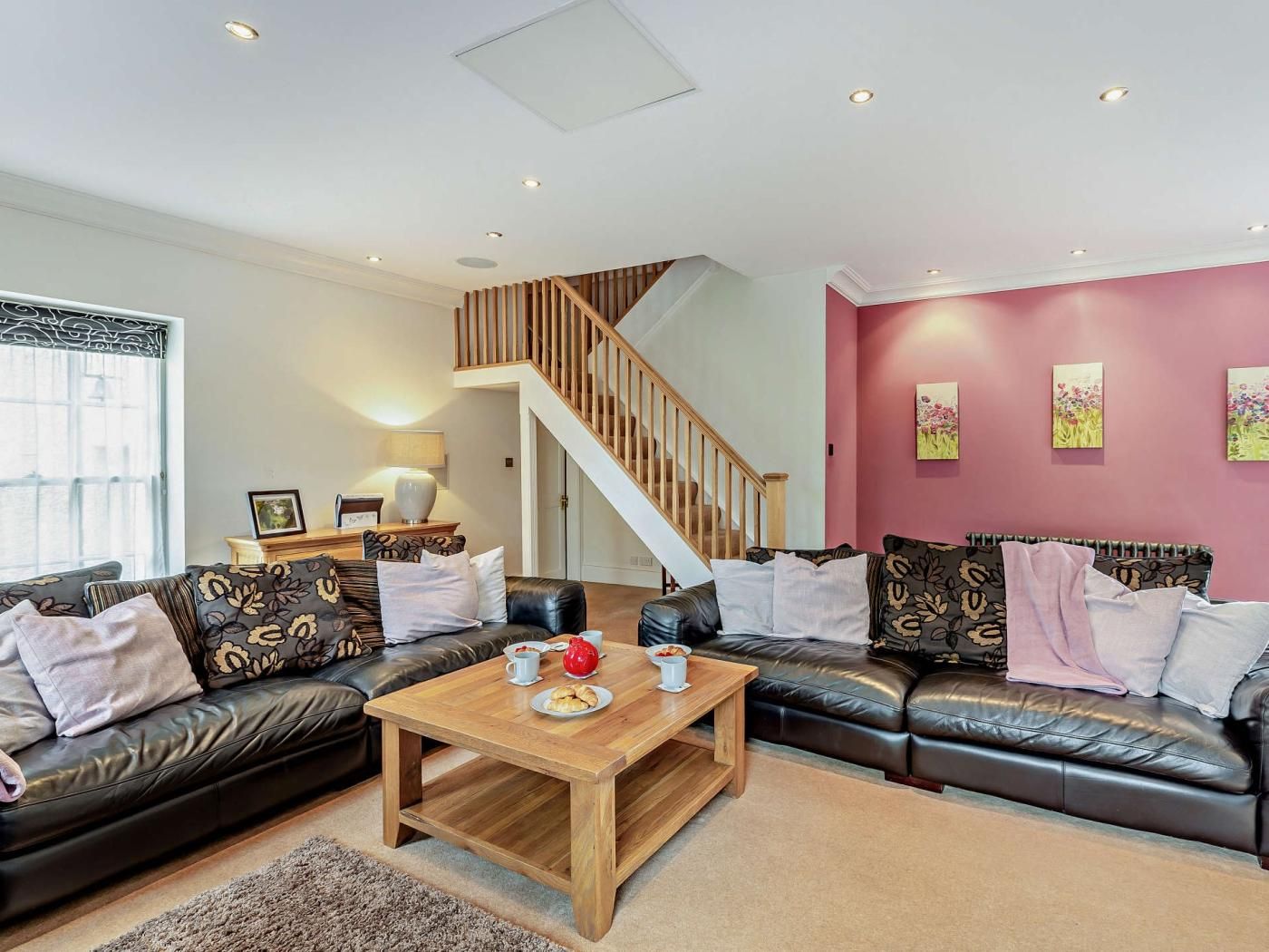 A modern living room with a wooden staircase, leather sofas, a coffee table, and artwork on the walls.