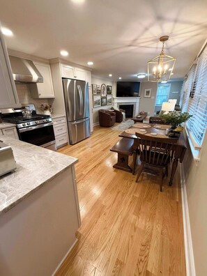 A modern kitchen with stainless steel appliances, a dining area with a wooden table and chairs, and a living space with a fireplace. - Newly renovated 2bed/2 bath, pet friendly, easy walk to village! (Skaneateles)