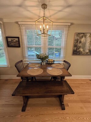 A dining area with a wooden table, four chairs, a chandelier, and a painting on the wall. - Newly renovated 2bed/2 bath, pet friendly, easy walk to village! (Skaneateles)