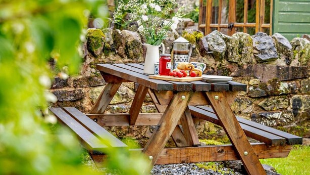 A rustic wooden picnic table with a vase of flowers, a teapot, and pastries. - 3 Bed in Wigton (oc-92826) (Torpenhow)
