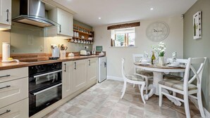 A modern kitchen with white cabinetry, a built-in oven, and a dining area with a round table and chairs. - 3 Bed in Wigton (oc-92826) (Torpenhow)