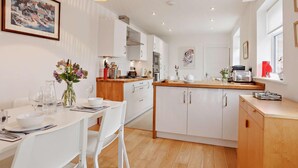 A modern kitchen with white cabinetry, a wooden countertop, and a dining area with white chairs. - 3 Bed in Bideford (oc-92882) (Bideford)
