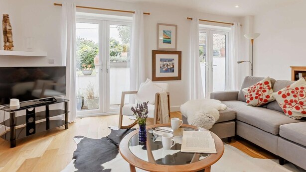A modern living room with a sofa, a glass coffee table, a TV, and a dining area with a glass table and chairs. - 3 Bed in Bideford (oc-92882) (Bideford)