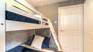A bunk bed with a brick wall and striped wallpaper, a white door, and a wooden floor. - 2 Bed in Seahouses (oc-92880) (Seahouses)