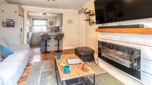 A living room with a sofa, coffee table, and fireplace. There is a kitchen in the background with a dining area. - 2 Bed in Seahouses (oc-92880) (Seahouses)