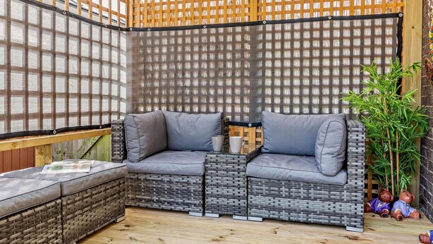 A corner seating area with a cushioned bench and a small table, surrounded by a wooden fence and a mesh screen. - 2 Bed in Seahouses (oc-92880) (Seahouses)