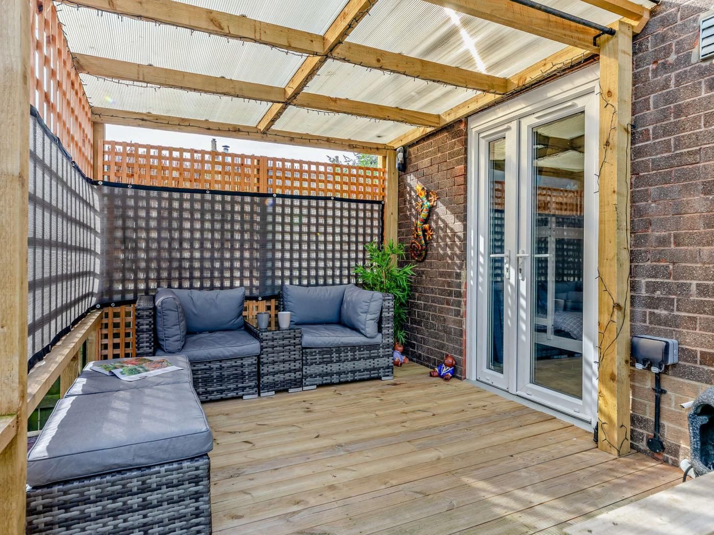 Un área de patio techada con un conjunto de asientos, una terraza de madera y un muro de ladrillo.