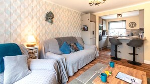 A living room with a sofa, a coffee table, and a kitchen area with a bar stool. - 2 Bed in Seahouses (oc-92880) (Seahouses)