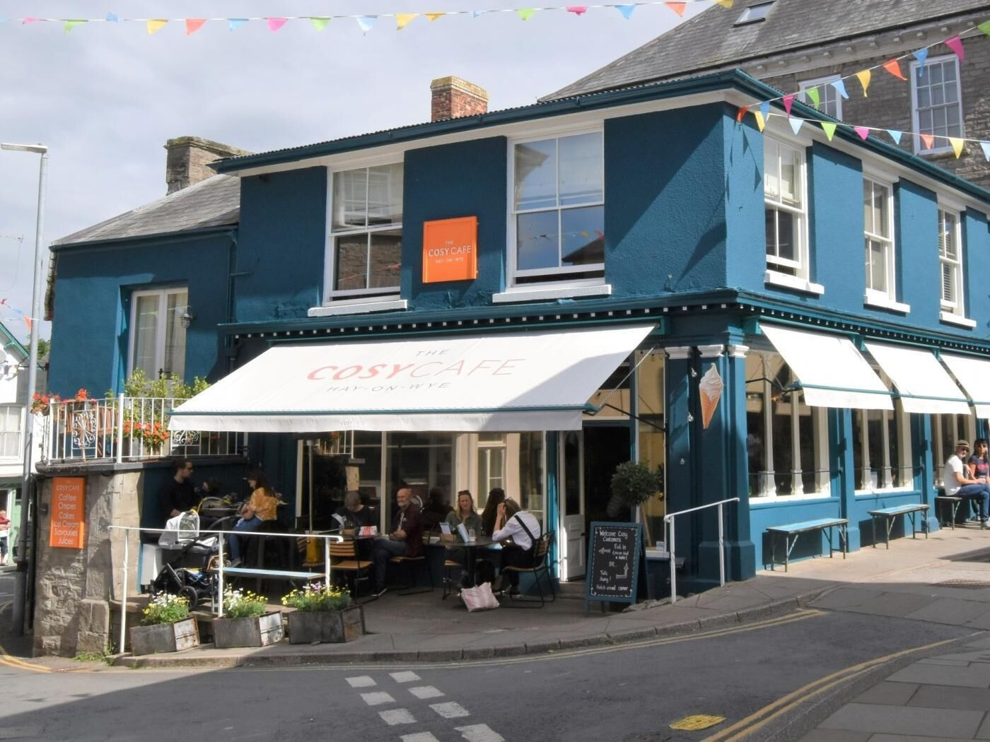 Ein blaues Gebäude mit einer weißen Markise, auf der 'The Cosy Cafe' steht.