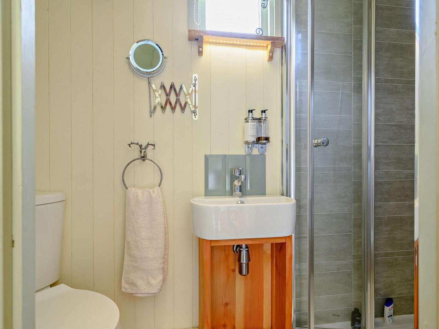 Une salle de bain comprenant des toilettes, un lavabo, un miroir, un porte-serviettes et une douche.