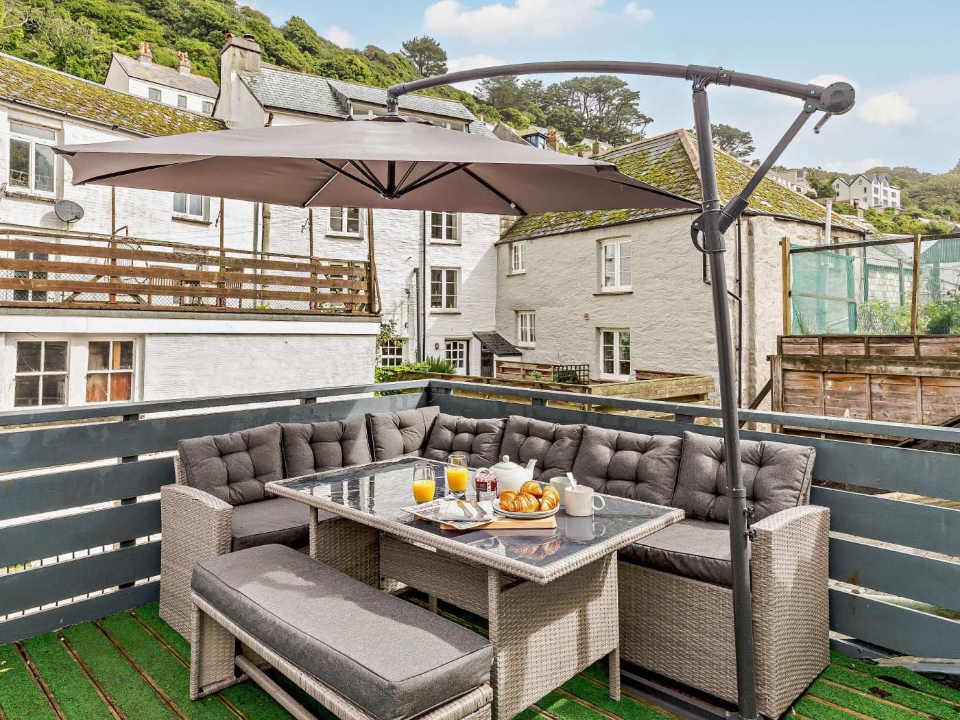 A balcony with a glass table, cushioned seating, and a large umbrella.