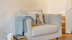 Un soggiorno moderno con una poltrona grigia, una coperta azzurra, una tazza bianca e un libro su un tavolino di legno.