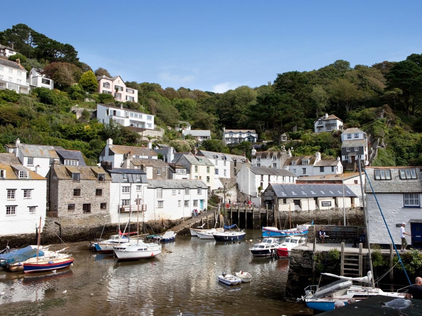 A coastal village with traditional stone buildings, a harbor with various boats, and a hillside with residential houses.