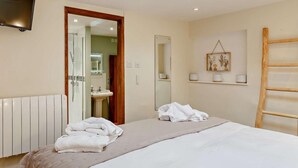 Una camera da letto con un letto, una TV, un bagno con uno specchio e una scala in legno.