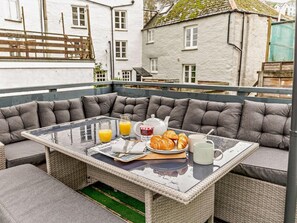 A dining area with a glass table, grey cushioned seating, and breakfast items including croissants, a teapot, and a cup. - 2 Bed in Looe (oc-92919) (Polperro)