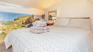 Une chambre à coucher avec un lit, des oreillers, une table de chevet, un vase avec des fleurs et un tableau encadré.