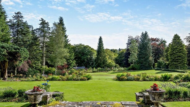 A well-maintained garden with a lawn, stone pathway, and two stone planters with flowers. - 2 Bed in Blairgowrie (oc-92998) (Alyth)