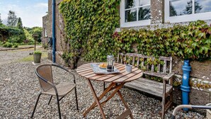 A stone building with ivy-covered walls, a wooden table with chairs, and a gravel patio. - 2 Bed in Blairgowrie (oc-92998) (Alyth)
