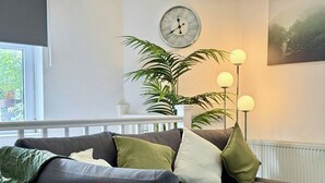 Un sofá gris con varios cojines, una planta en maceta, una lámpara de pie y un reloj en la pared.