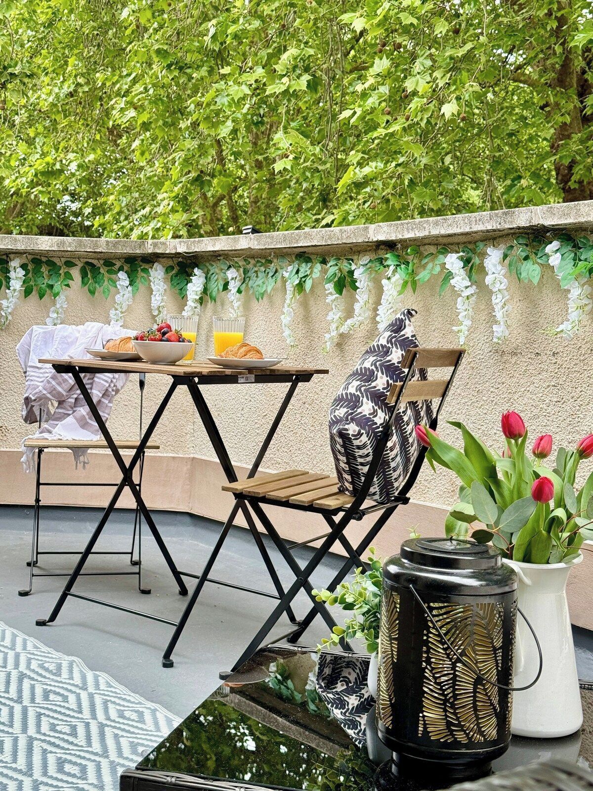 A dining area with a table set for two, a chair, a decorative wall, and a potted plant with red flowers.