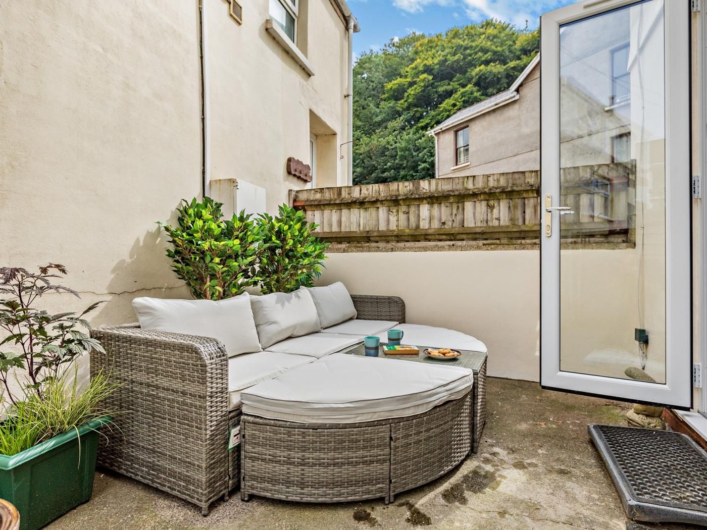 A corner patio with a wicker sofa, a small table, and potted plants.