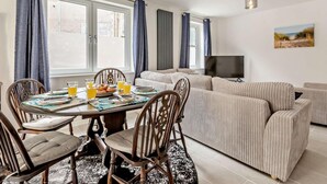 Uma sala de estar moderna com uma mesa de jantar, cadeiras, um sofá e uma televisão.