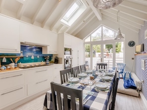 A modern kitchen with white cabinets, a dining area with a checkered tablecloth, and a large window. - 4 Bed in Bideford (oc-93051) (Appledore)