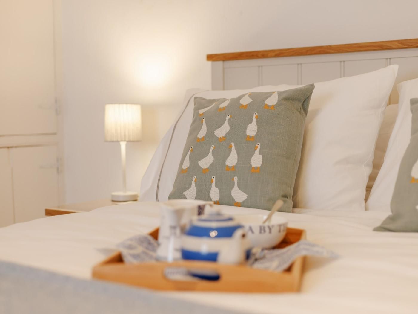 A neatly made bed with pillows, a bedside lamp, and a tray with a baby bottle and a cup.