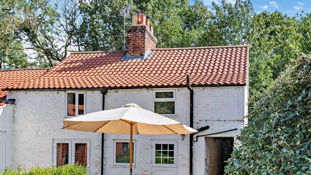 A white building with a red-tiled roof, a patio with a table and chairs, and a large umbrella. - 2 Bed in Driffield (oc-93141) (Langtoft)